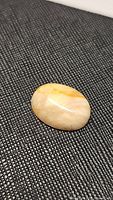 Oval cabochon golden opal gemstone on textured black surface, showing smooth polished top and natural color variations.
