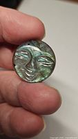Close-up of hand holding a round carved labradorite stone with carved face design showing blue-green flash.