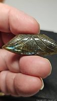 Close-up front view of hand holding the carved labradorite showing golden blue flash and feather design.