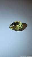 Single natural lemon citrine gemstone pear cut photographed on neutral background showing facets and clarity.