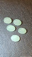 Five oval cabochon cut natural mint green kyanite stones displayed on a textured surface, showing color, size and internal texture.