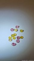 Top down photo of natural mixed yellow and pink tourmaline gemstones scattered on white background, showing size, shape and colors of stones