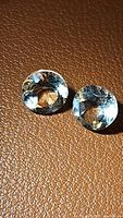Two round cut natural prasiolite (green amethyst) gemstones with excellent clarity placed on a brown textured surface under good lighting to highlight color and facets.