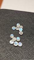 Close-up of 11 natural round cabochon rainbow moonstone gems on black fabric showing blue flashes.