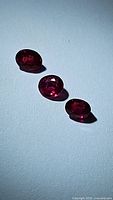 Three natural pigeon blood red rubies arranged linearly on a white surface, showing color and cut.