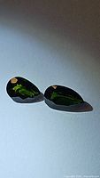 Two pear-shaped natural green chrome diopside stones on a white background showing color and shape.