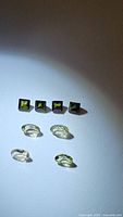 Photo of four square-cut dark green Tourmaline gemstones and two oval-cut light green Tourmaline stones on white background under light.