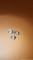 Three pear-shaped aquamarine gemstones displayed on a brown surface under natural light, showing clarity and cut.