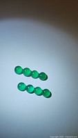 Eight small round cabochon vivid green onyx gemstones arranged in two rows on white background, showing smooth polished surfaces and bright green color.