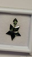 Photo of blue green kite cut sapphire pendant in display box, showing star pattern formation of the gemstones.