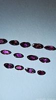 Thirteen marquis cut untreated rubies shown from an angle with reflection and clear lighting illustrating their colors and shapes.