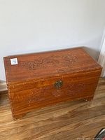 Front view of carved Chinese camphor wood chest showing top dragon and phoenix carvings, lock hardware, and overall wear on wood surface.