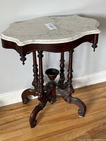 Front angle showing the marble top and dark carved wood base with turned legs and central urn accent
