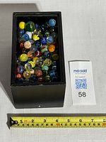 Black rectangular box filled with vintage glass marbles of assorted colors and patterns, measuring approximately 6 inches long