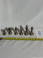 Full set of 6 stainless steel chess puzzle pieces aligned in a row with a measuring tape for scale. Pieces are shiny and polished with a substantial weight.