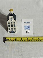 Front view of the ceramic house next to a measuring tape and lot number card showing height approx 10cm