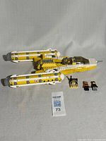 Full view of yellow and white LEGO Star Wars Y-Wing Starfighter with cockpit canopy detached and three minifigures standing beside it on the floor.