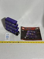 Purple triple-decker Knight Bus Lego set 4866 posed next to instruction booklet and measuring tape indicating about 13 inches long