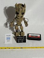 Full view of I Am Groot Lego figure standing on black base next to a cassette tape for size reference.