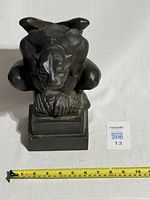 Front view of the cast iron gargoyle with a measuring tape showing approximately 7 inches width.