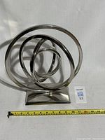 Front angled view of chrome spiral ring sculpture with tape measure showing width approximately 10 inches.
