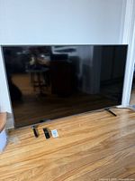 Front view of Samsung 55-inch TV on stand legs with remote on floor
