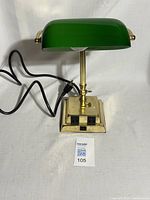 Front view of a vintage brass bankers desk lamp with emerald green glass shade. Brass base and stem, black cord, two black switches on base.