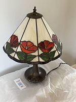 Full view of stained glass lamp showing floral pattern on cream background and brass base