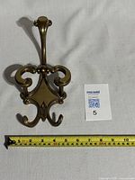 Front view of the vintage brass wall hanger with measuring tape showing approximately 10 inches height.
