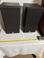 Two vintage bookshelf speakers covered by black fabric grilles, standing upright, showing overall size and appearance.