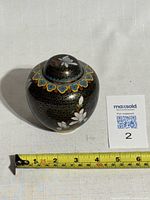 Top front view showing the domed lid with multicolored floral design band and black background with gold cloud patterns and white flowers on the jar body.