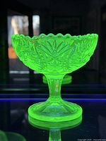 Photo of smaller uranium glass dish glowing bright green under UV light, showing starburst pattern and scalloped edge.