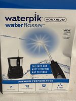 Front of Waterpik Aquarius water flosser box showing product name, features, 7 tips included, 10 pressure settings, 90 second water capacity, and warranty details.