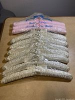 Ten white satin-covered padded hangers laid out, showing both front and side views with metal hooks.