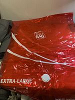 Photo of a red extra-large vacuum seal bag with a white valve, laid flat on gray surface.