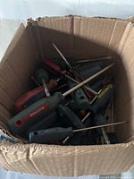 Top-down view of assorted screwdrivers of various sizes and handle colors inside a cardboard box.