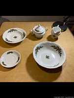 Photo of white ceramic dishes featuring holly berry, green leaf holiday Christmas pattern, includes sugar bowl with lid, creamer pitcher, two bowls, and a small dish.