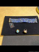 Photo showing blue beaded bracelet and two rings on black display surface