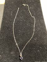 Full view of silver-tone chain necklace with square purple cubic zirconia pendant on black background.