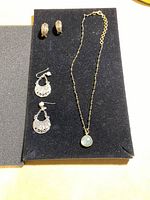 Full view of necklace and three pairs of earrings on black display pad