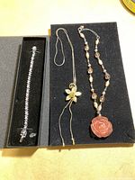Photo showing all three pieces of jewellery on black display: silver rhinestone bracelet in box, gold-tone flower pendant necklace, and beaded necklace with peach rose pendant.