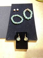 Overview of the costume jewellery set showing two bracelets, pearl-like stud earrings, and drop earrings with clear stones on black display pads.