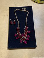 Full view of necklace and earrings on black background showing the design and colors of the teardrop stones.