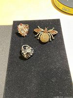 Photo of two rhinestone rings and a rhinestone bee brooch on black fabric