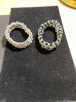 Photo showing two handcrafted bracelets on a black cloth, one with clear beads and one with dark green beads, both woven with silver-toned wire.