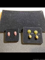 Two pairs of earrings on black display: pink rhinestone hoops and green rhinestone studs with hanging pearls.