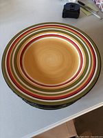 Stack of 8 large multicolored concentric circle striped plates with visible colors of tan, red, cream, olive green, and black.
