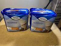 Two unopened packages of TENA Ultimate Protective Underwear, Large size, placed side by side showing front and side views with product branding and absorbency level visible.