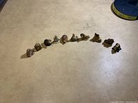 Wide angle showing all 10 small figurines arranged in a line on a beige surface under lighting.