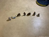 Shows all seven small figurines lined up on a flat surface, displaying their size and detail.